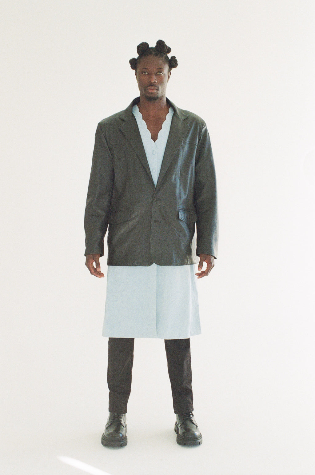 Person wearing a black jacket over a light blue shirt with a white skirt on a white background