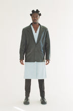 Person wearing a black jacket over a light blue shirt with a white skirt on a white background