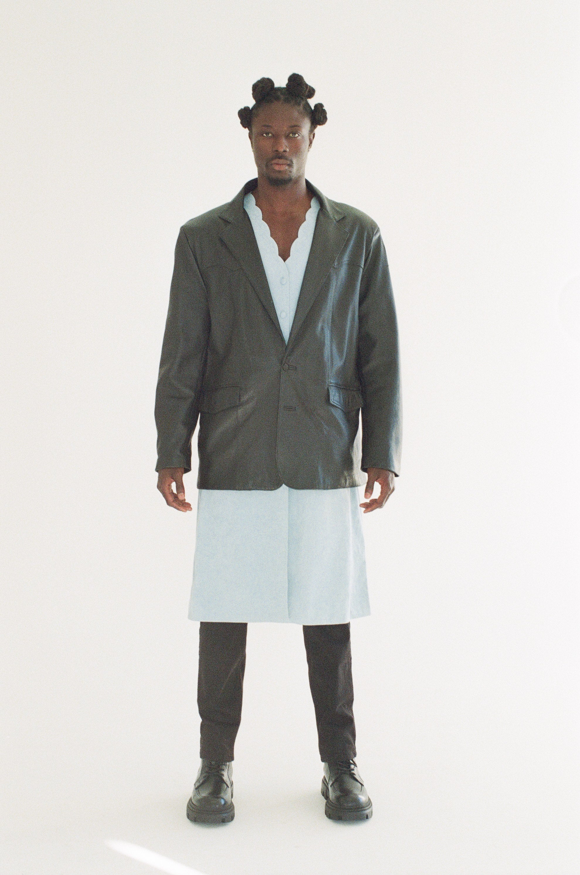 Person wearing a black jacket over a light blue shirt with a white skirt on a white background