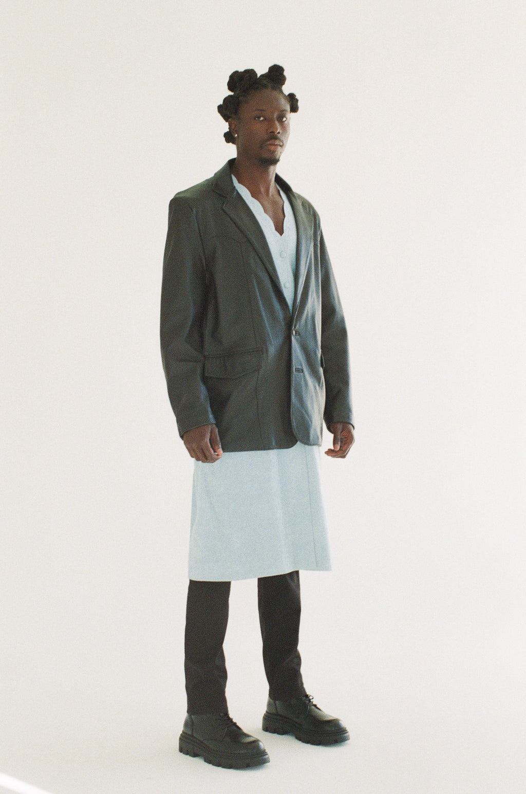 Man wearing a long black blazer over a white shirt on a white background