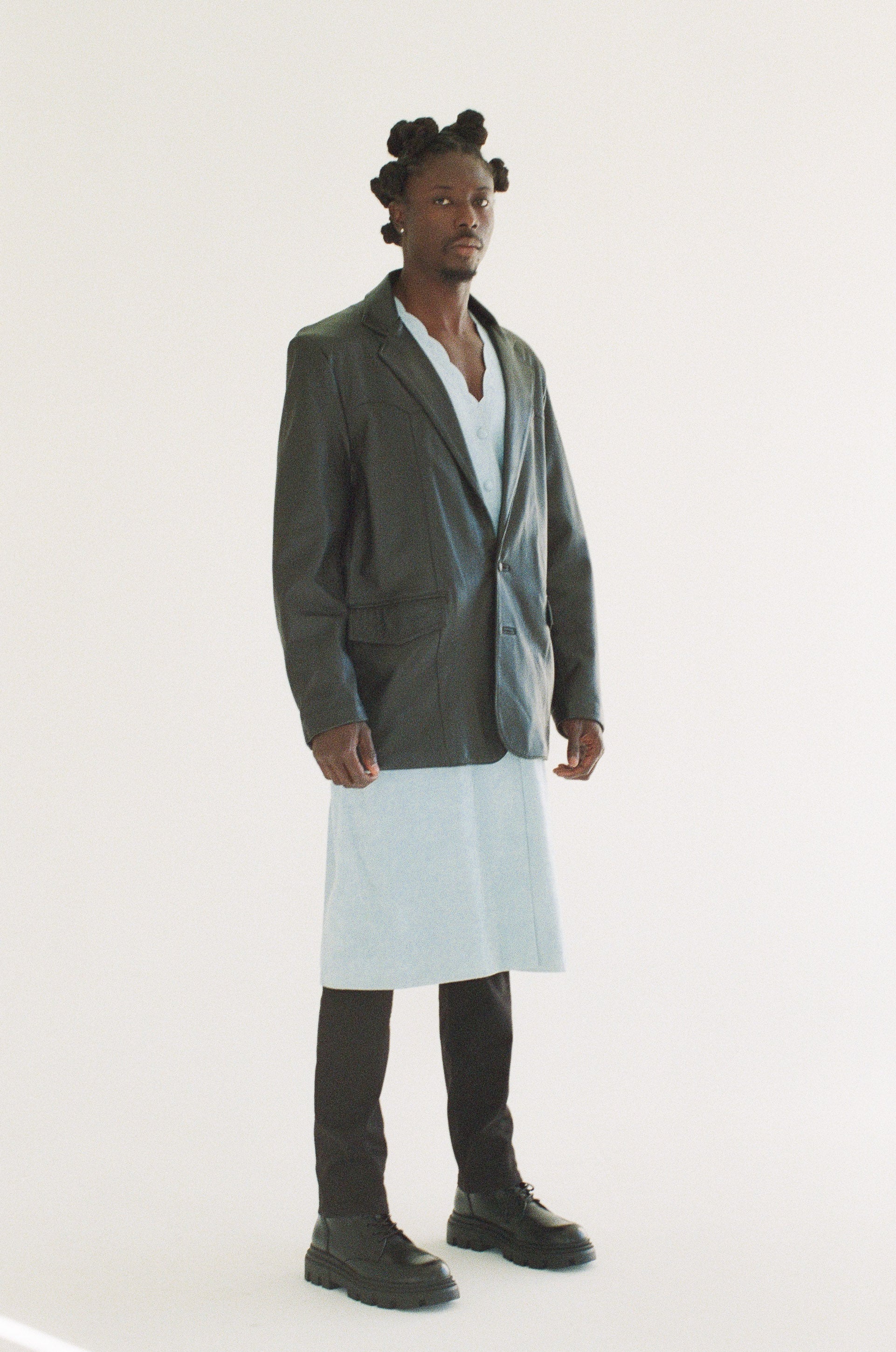 Man wearing a long black blazer over a white shirt on a white background