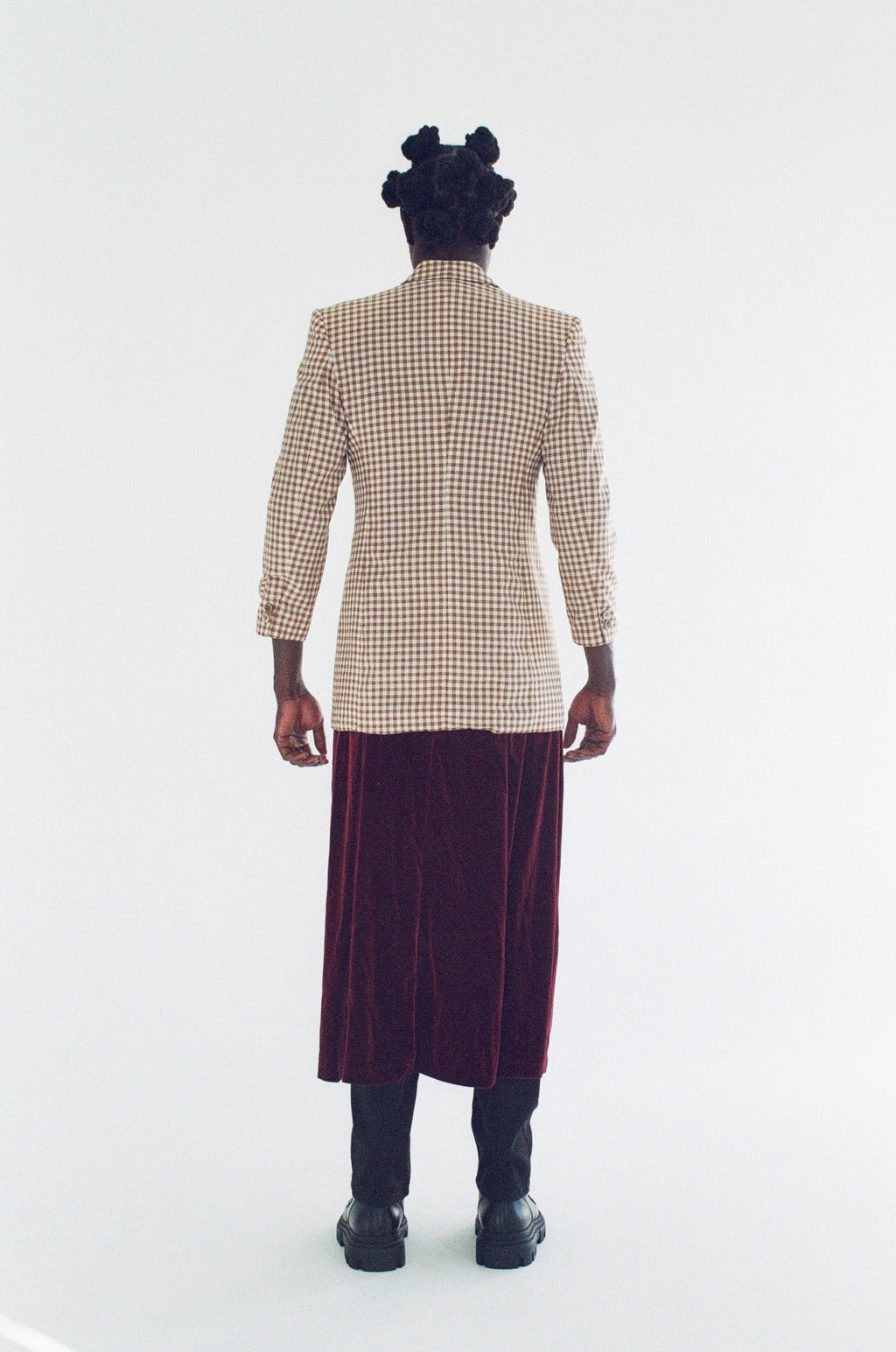 Person wearing a checkered blazer and purple skirt on a white background