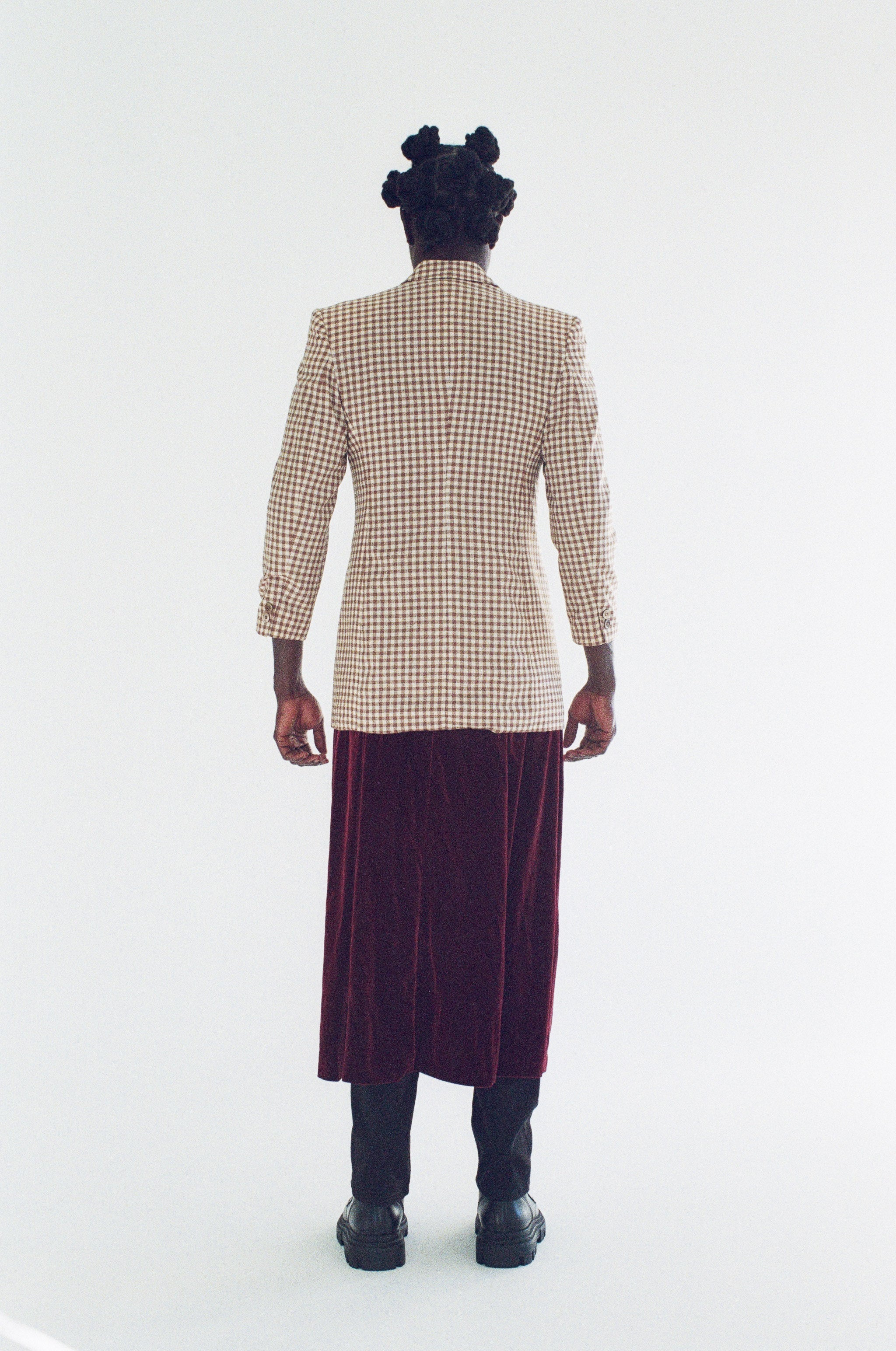 Person wearing a checkered blazer and purple skirt on a white background