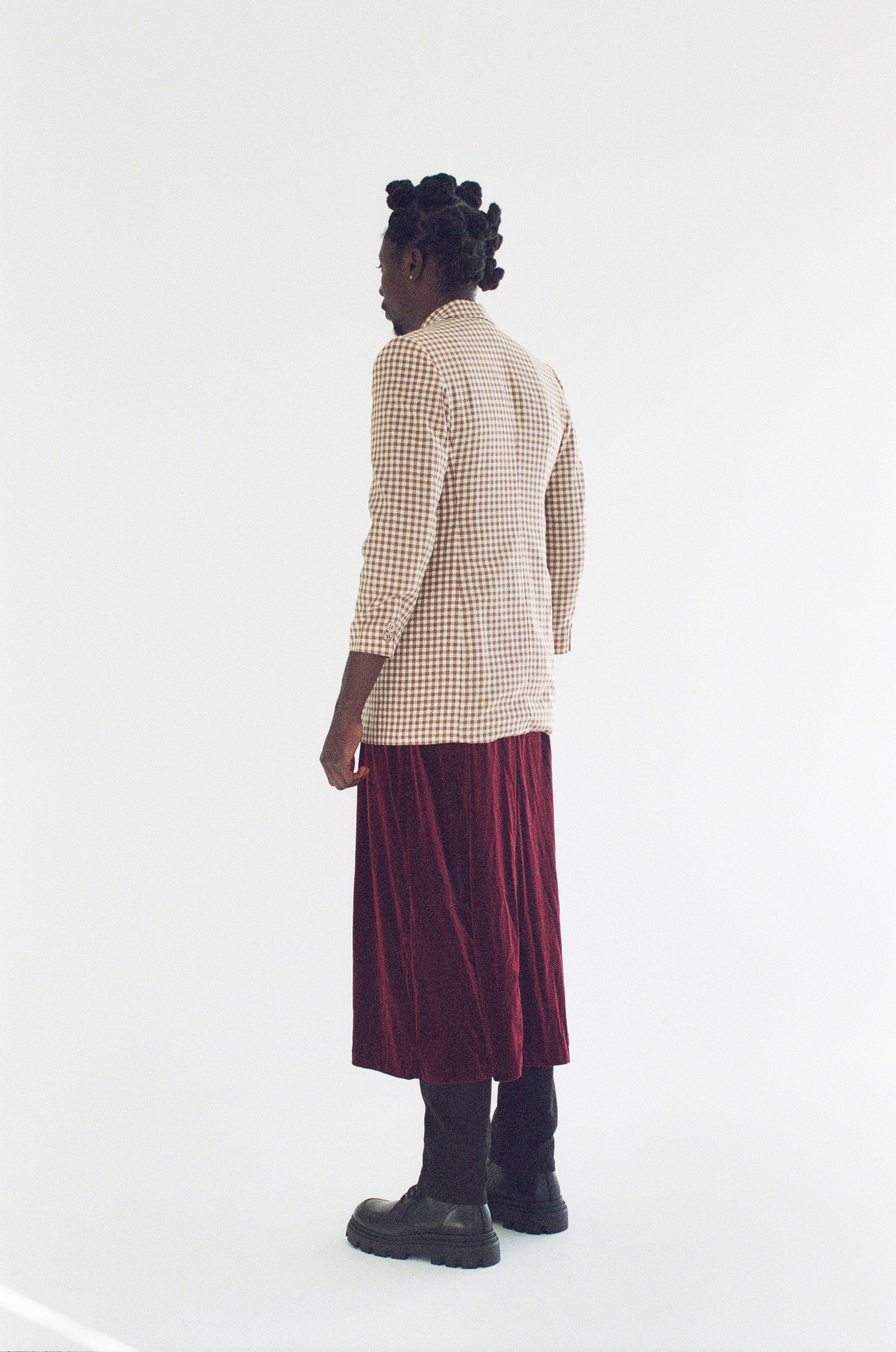 Person wearing a beige checkered shirt and burgundy skirt on a white background