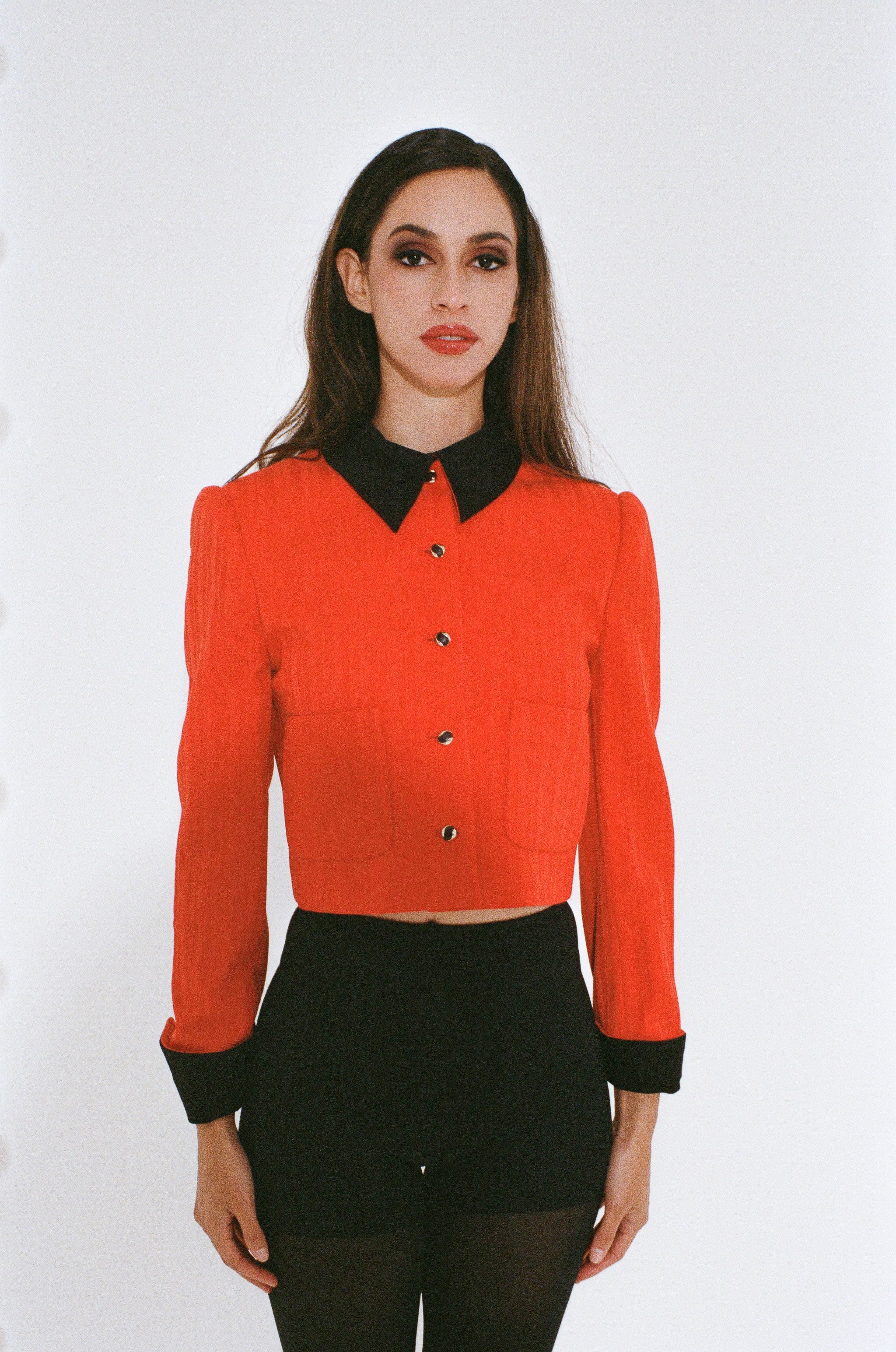 Woman wearing a red blouse with black collar and cuffs on a white background