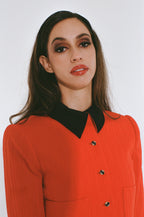 Woman wearing a red outfit with a black collar against a white background