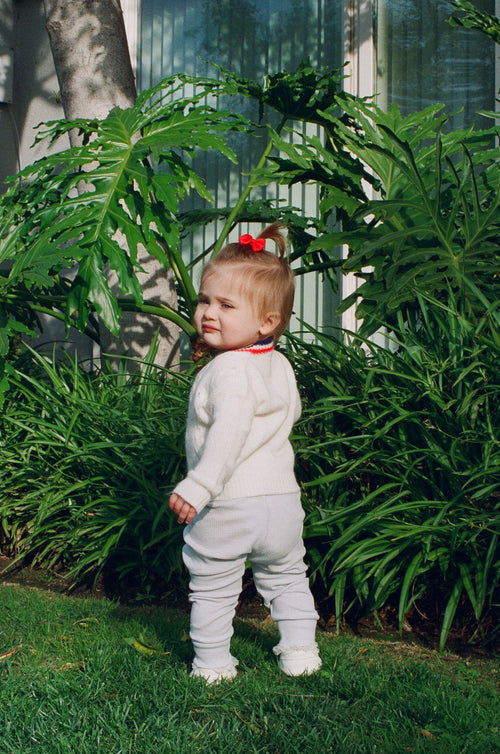 Child in a white outfit standing among green plants