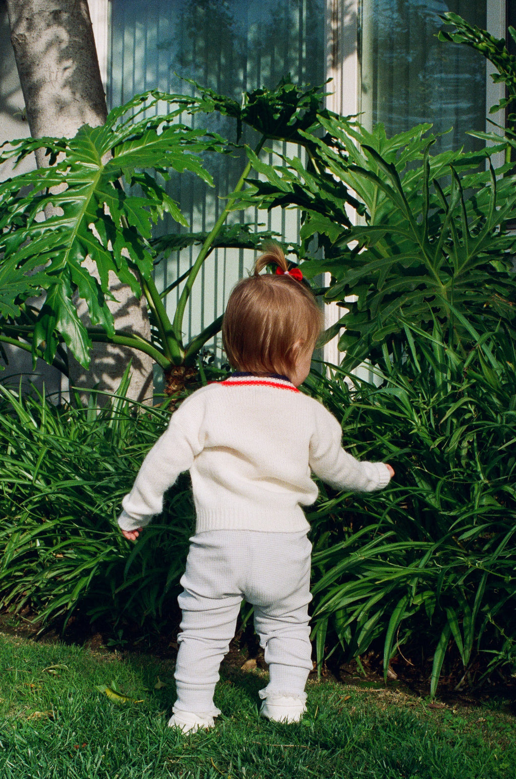 Child in a white outfit standing among green plants outdoors