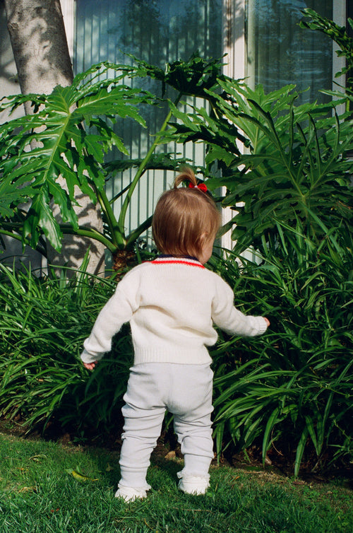 Child in a white outfit standing among green plants outdoors