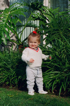 Child in a white sweater and pants standing among green plants