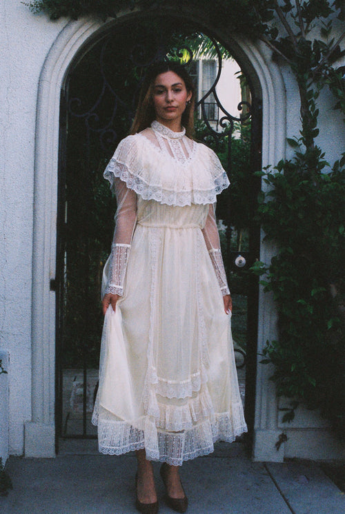 Woman in a white lace dress standing in front of a door with greenery.