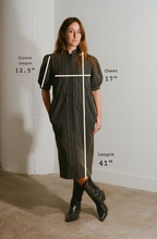 Woman wearing a dark green dress with measurements indicated on a plain background