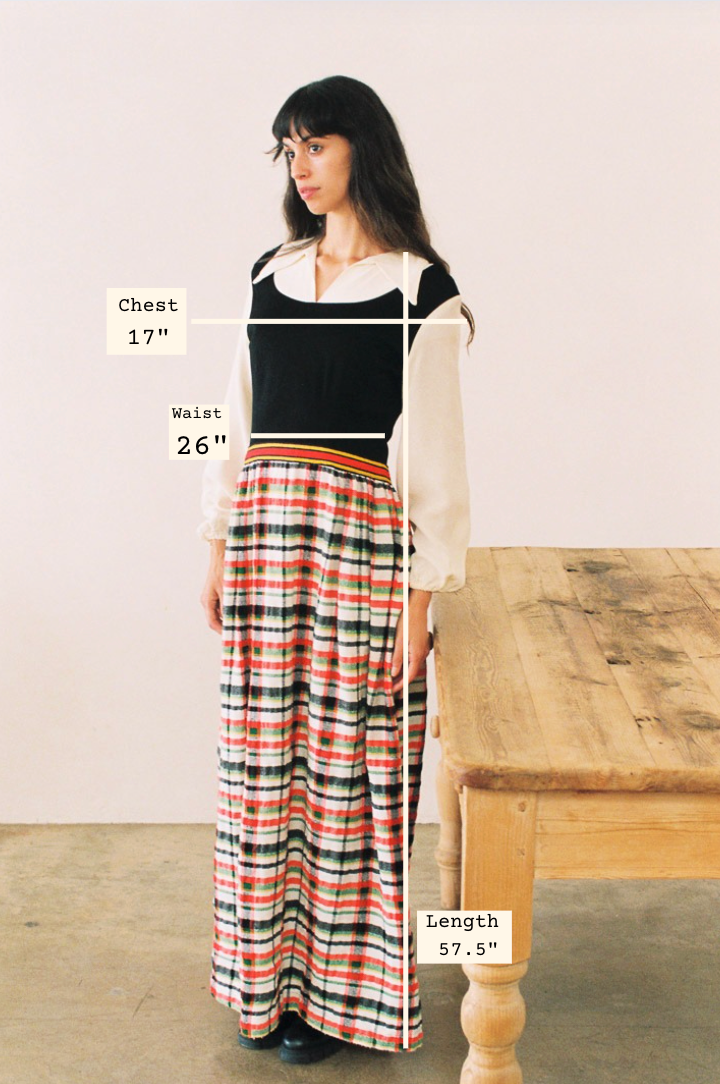 Woman wearing a long dress with measurements labeled, standing next to a wooden table.