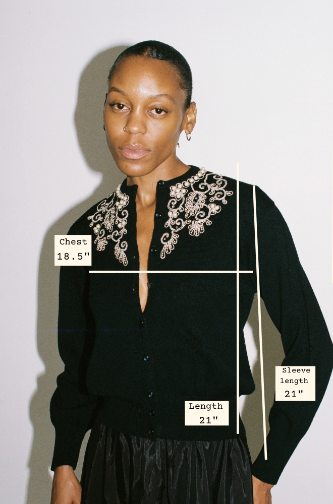 Woman wearing a black cardigan with white embroidery, shown with measurements on a plain background.