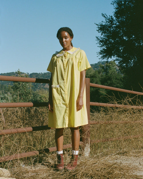 Woman in a yellow dress standing outdoors with trees and clear sky in the background