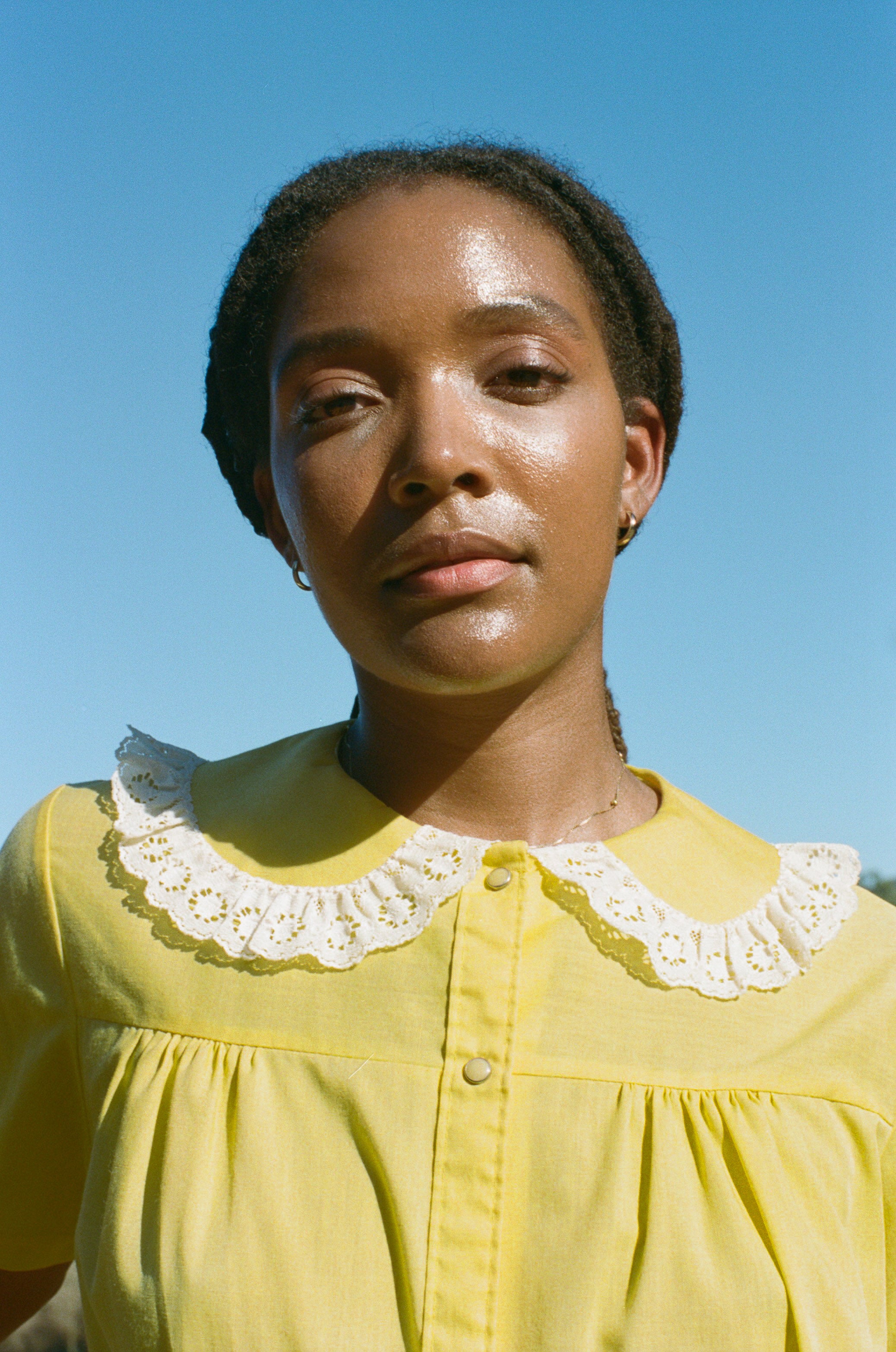 Woman wearing a yellow blouse with a white lace collar against a clear blue sky.