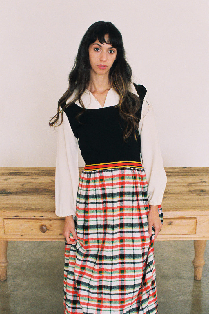 Woman wearing a black top with a white shirt and plaid skirt in front of a wooden bench.