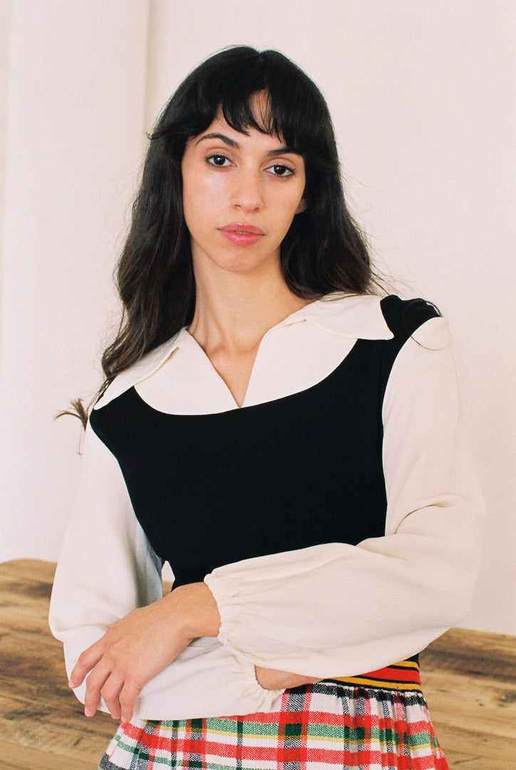 Woman wearing a black and white outfit with a plaid skirt against a plain background