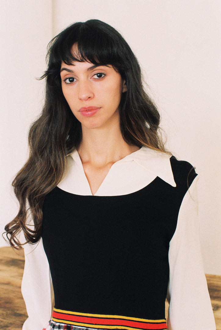 Woman wearing a black sleeveless top with a white collar and colorful trim against a neutral background