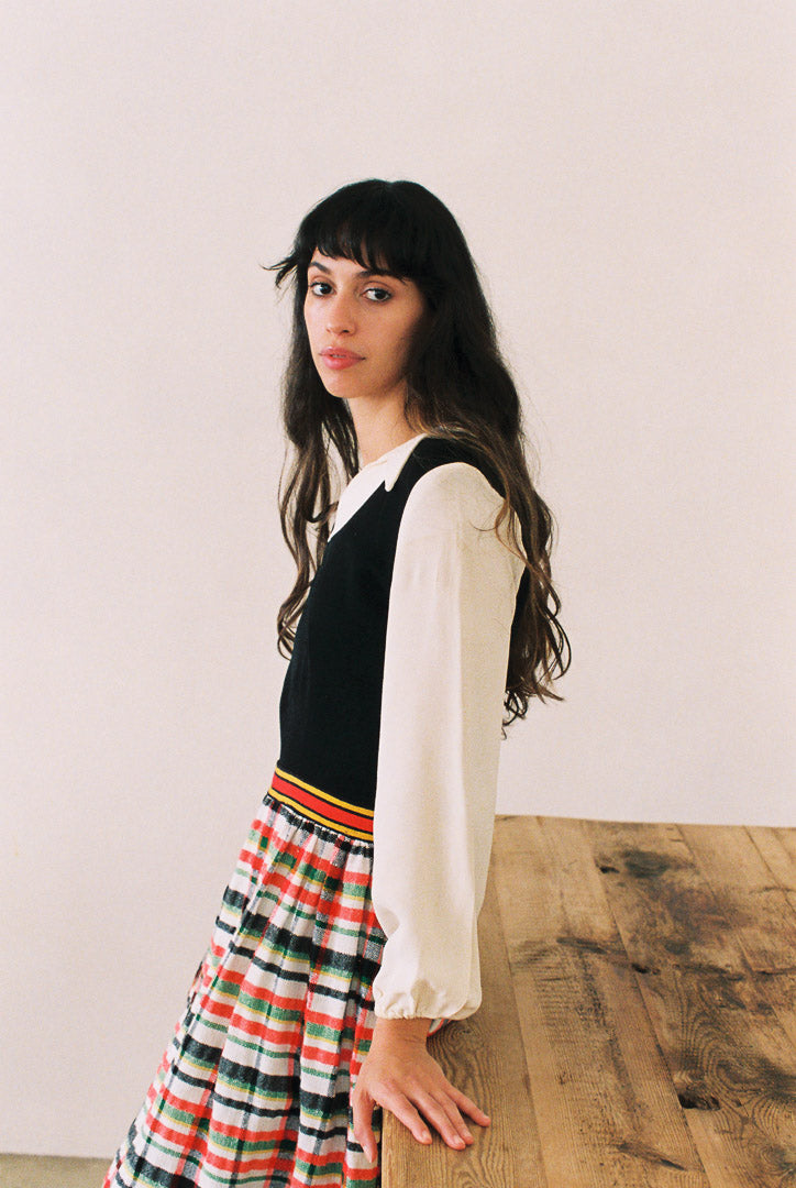 Woman wearing a black top with a white shirt and colorful skirt on a wooden floor.