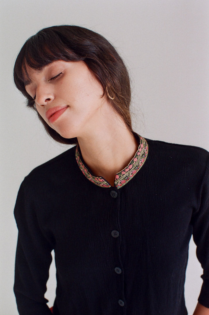 Woman wearing a black shirt with a patterned collar against a plain background