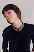 Woman wearing a black shirt with a patterned collar against a plain background