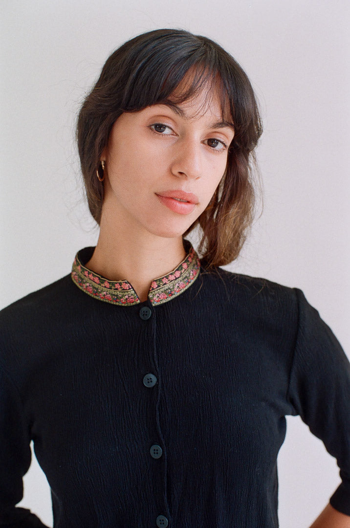 Woman wearing a black outfit with a patterned collar against a plain background