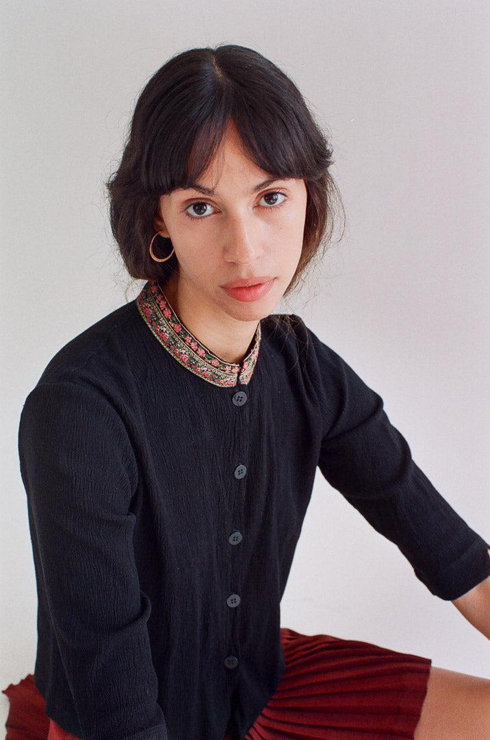 Person wearing a black cardigan with a patterned collar against a plain background