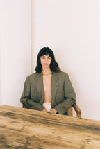 Woman sitting at a wood table wearing a pliad blazer and white skirt