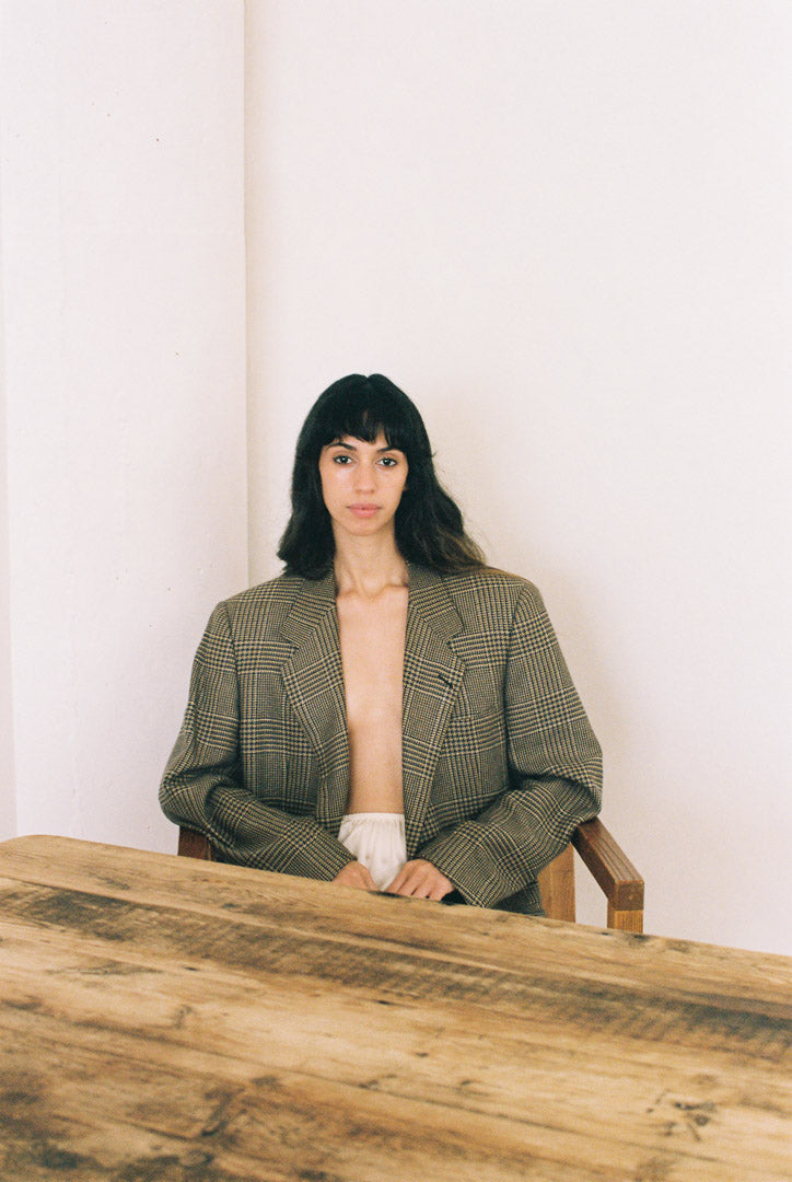 Woman sitting at a wood table wearing a pliad blazer and white skirt