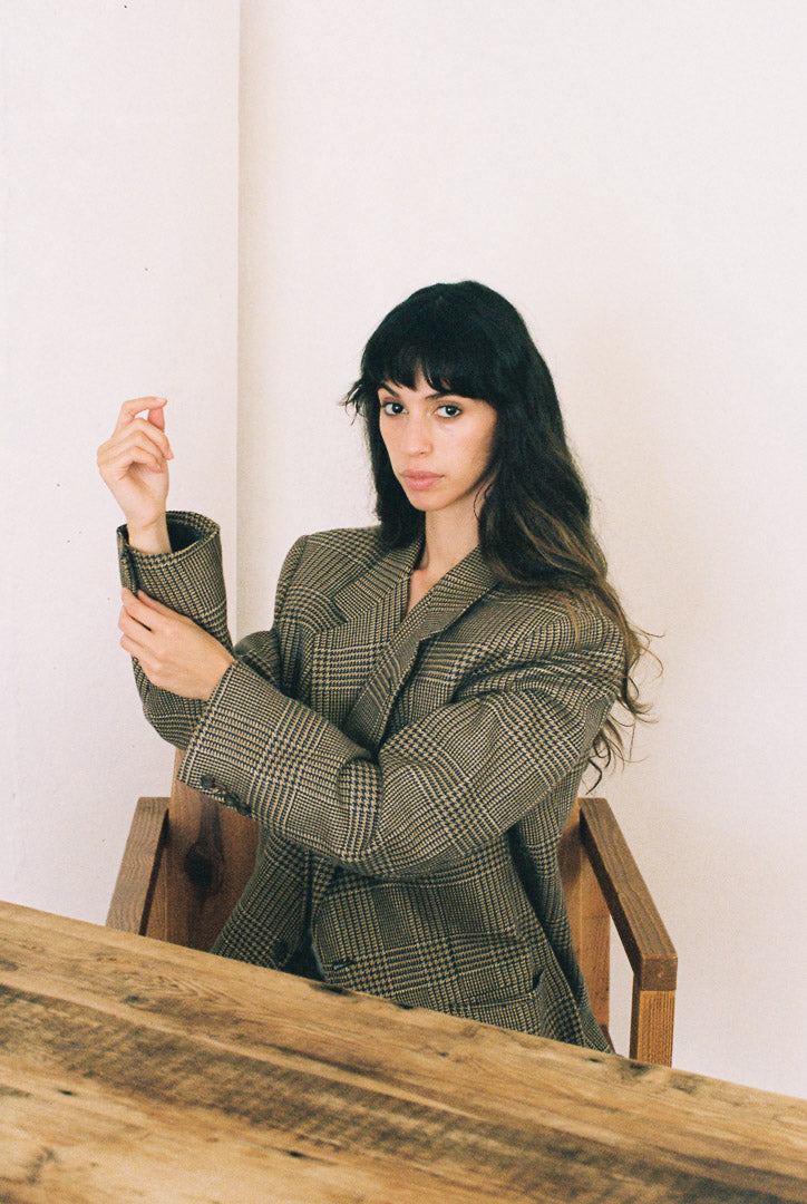 Woman in a plaid blazer sitting at a wooden table with a white background