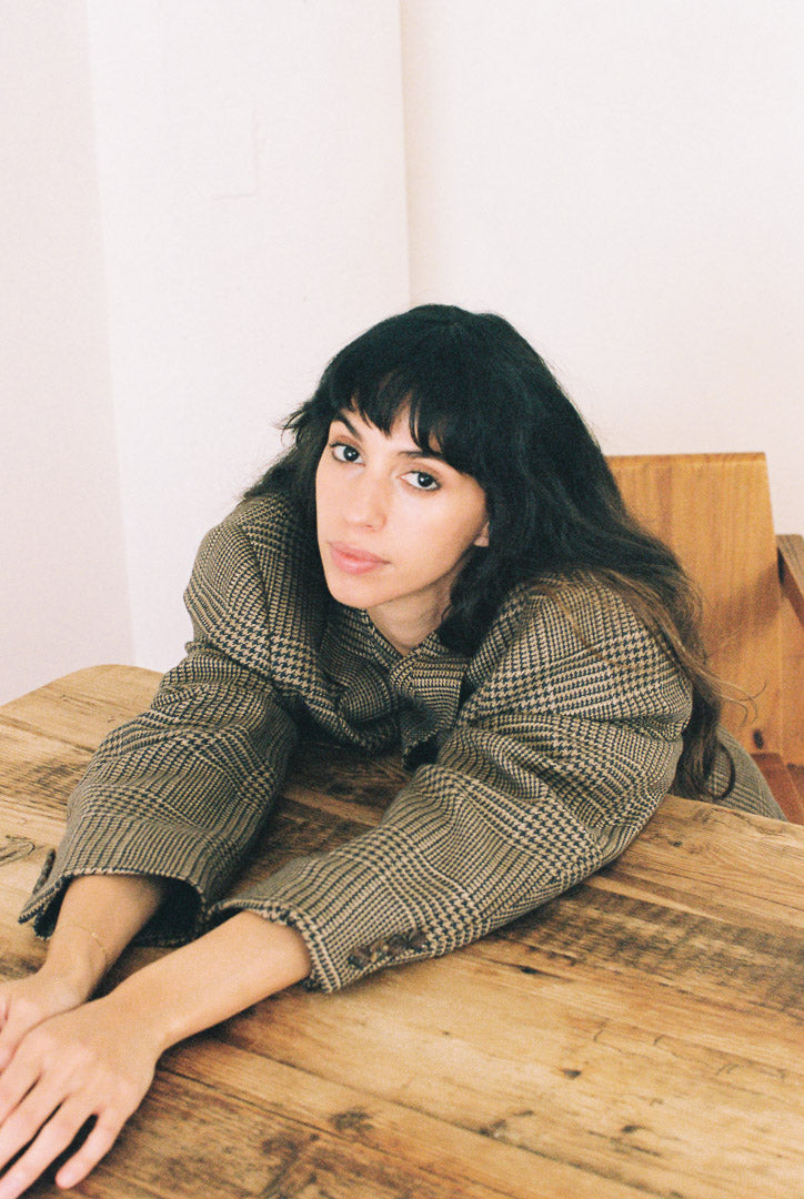 Woman in a plaid jacket sitting on a wooden table with a white background