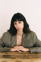 Woman wearing a plaid blazer sitting at a wooden table with a plain background