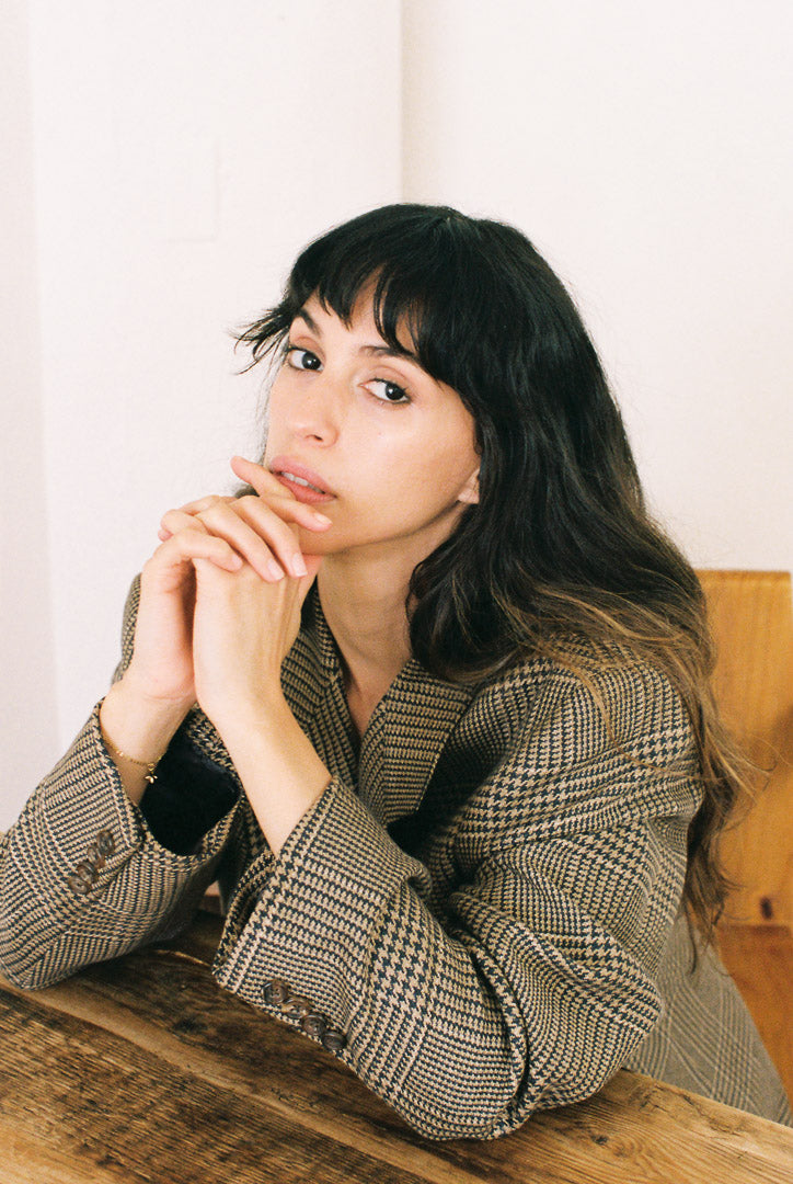 Woman sitting in a plaid blazer at a wooden table with a neutral background