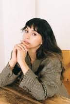 Woman sitting in a plaid blazer at a wooden table with a neutral background