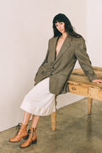 Woman wearing a green checkered blazer over a white skirt, sitting on a wooden bench.