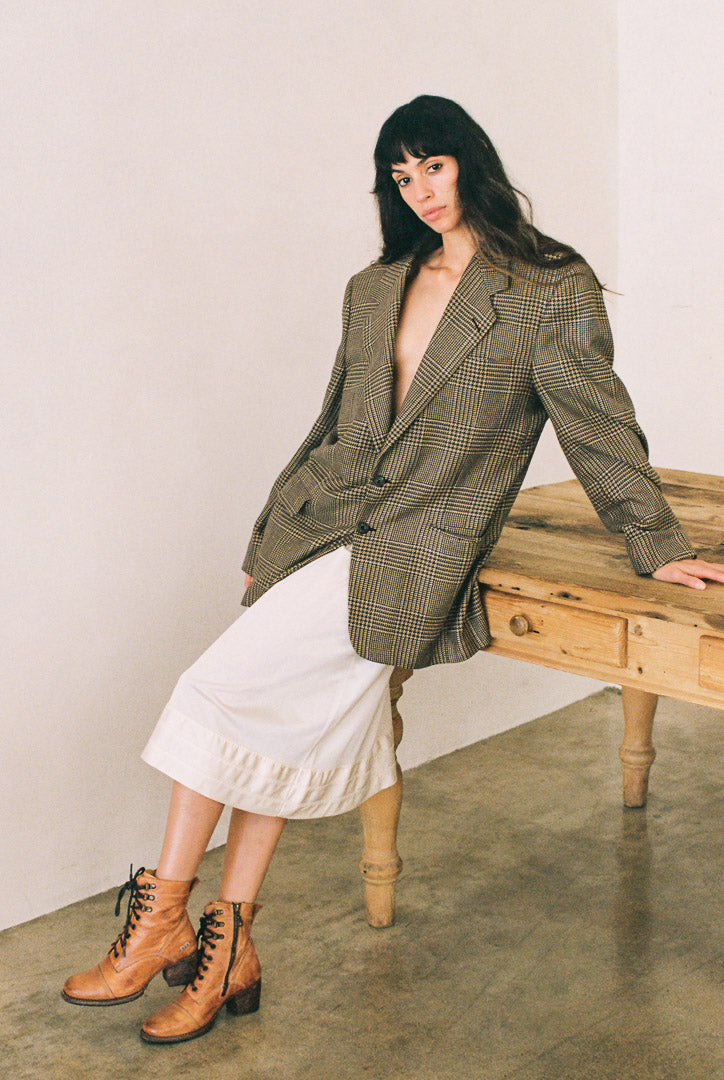 Woman wearing a green checkered blazer over a white skirt, sitting on a wooden bench.