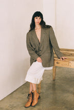 Woman wearing a green checkered blazer over a white top, standing against a plain wall.