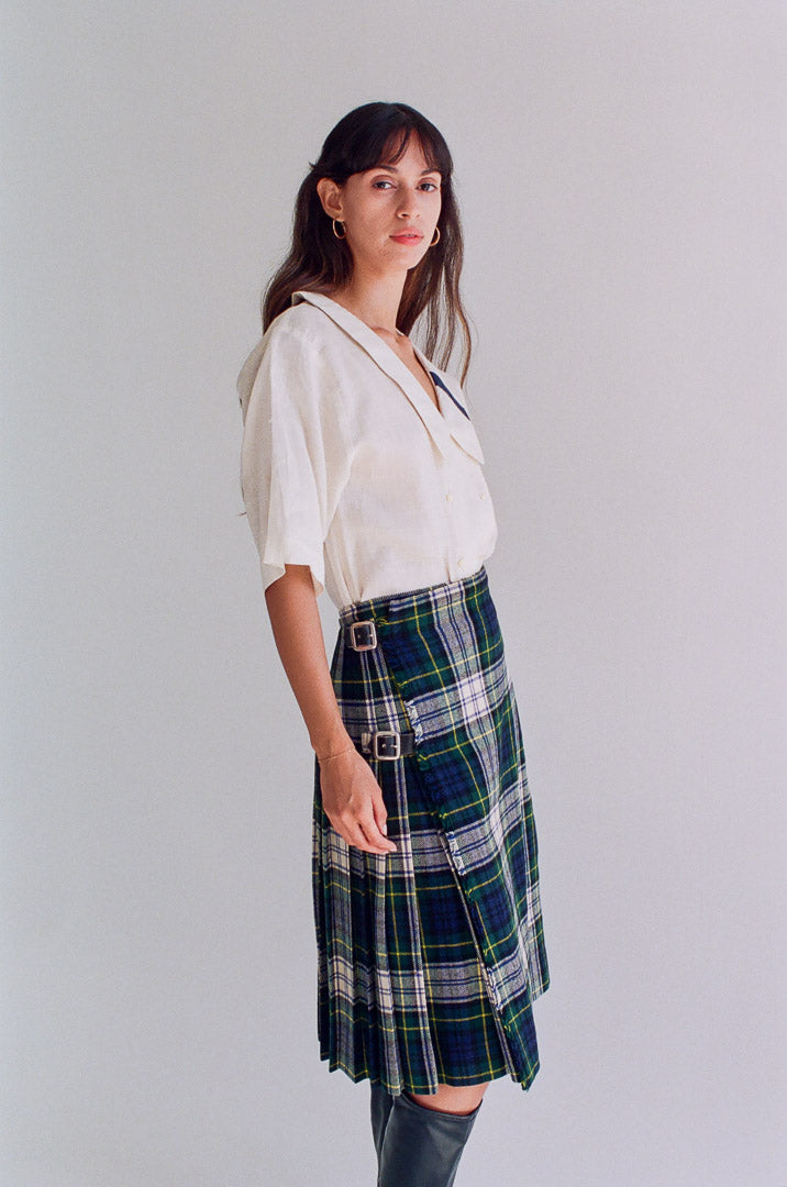 Woman wearing a white blouse and plaid skirt against a plain background