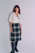 Woman wearing a white blouse with blue accents and a plaid skirt on a plain background