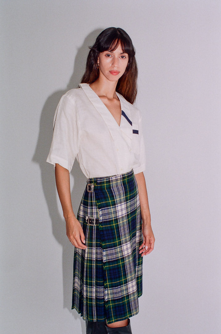 Woman wearing a white blouse and plaid skirt against a plain background