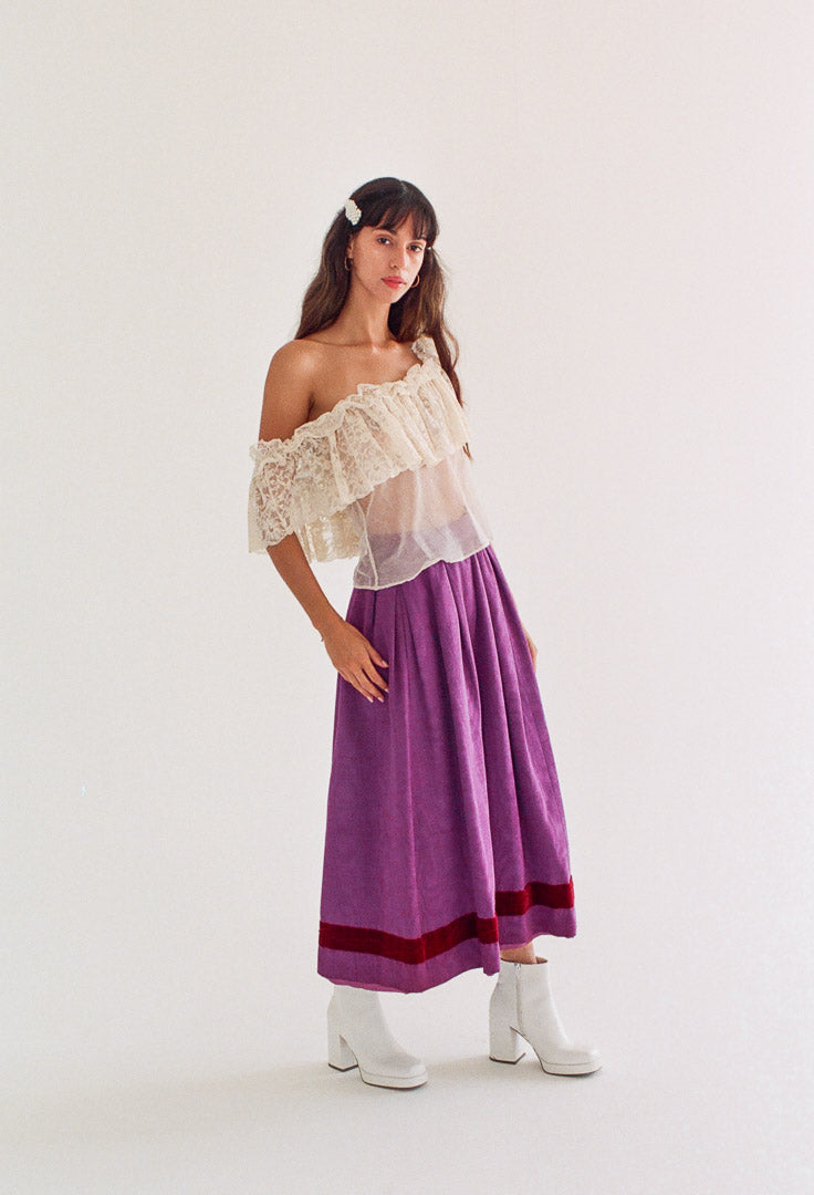 Woman wearing a white lace top and purple skirt on a white background