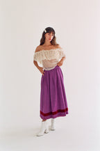 Woman wearing a white off-shoulder top and purple skirt on a white background