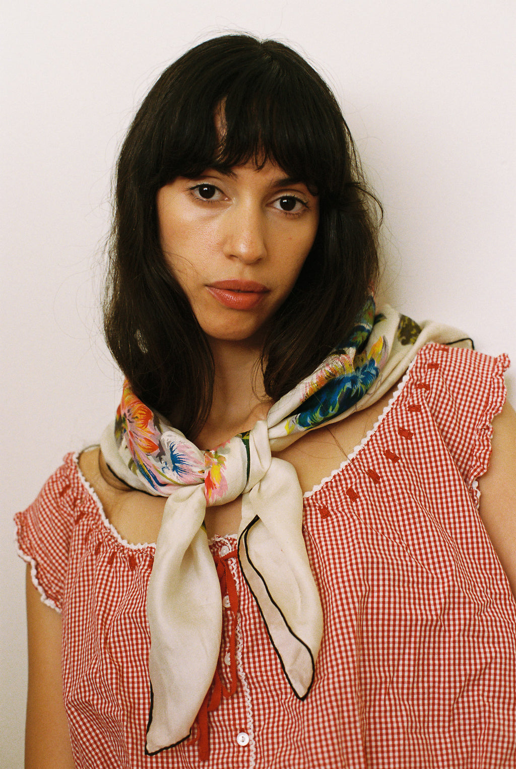 Woman wearing a colorful scarf and red checkered dress against a plain background