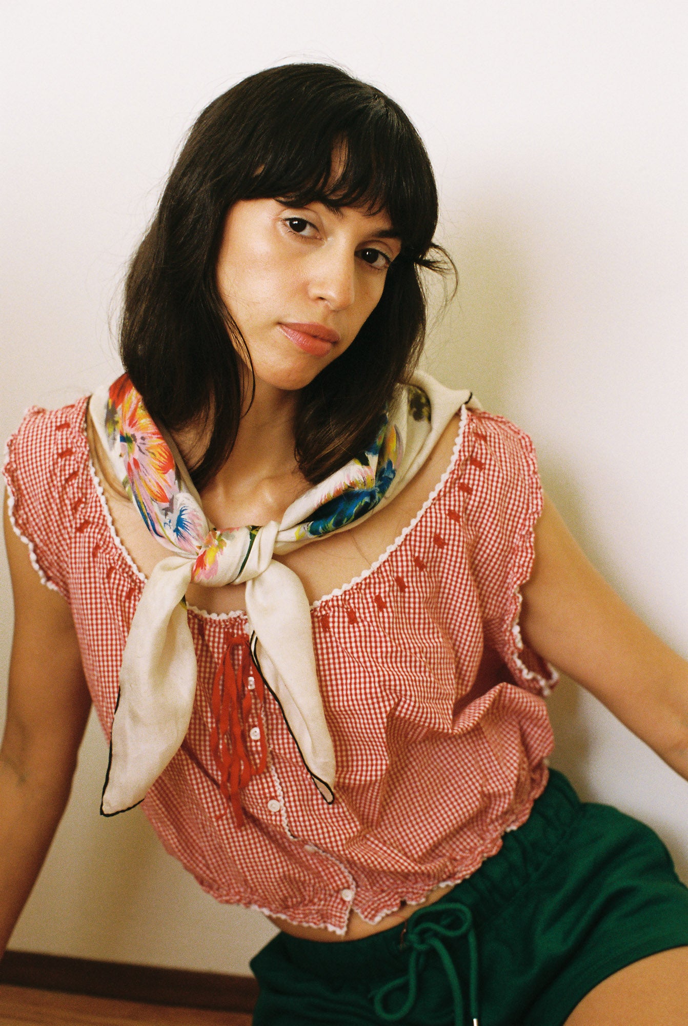 Woman wearing a red checkered top with a colorful scarf, sitting against a plain background