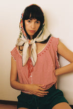 Woman wearing a red checkered top and green shorts with a colorful headscarf against a plain background
