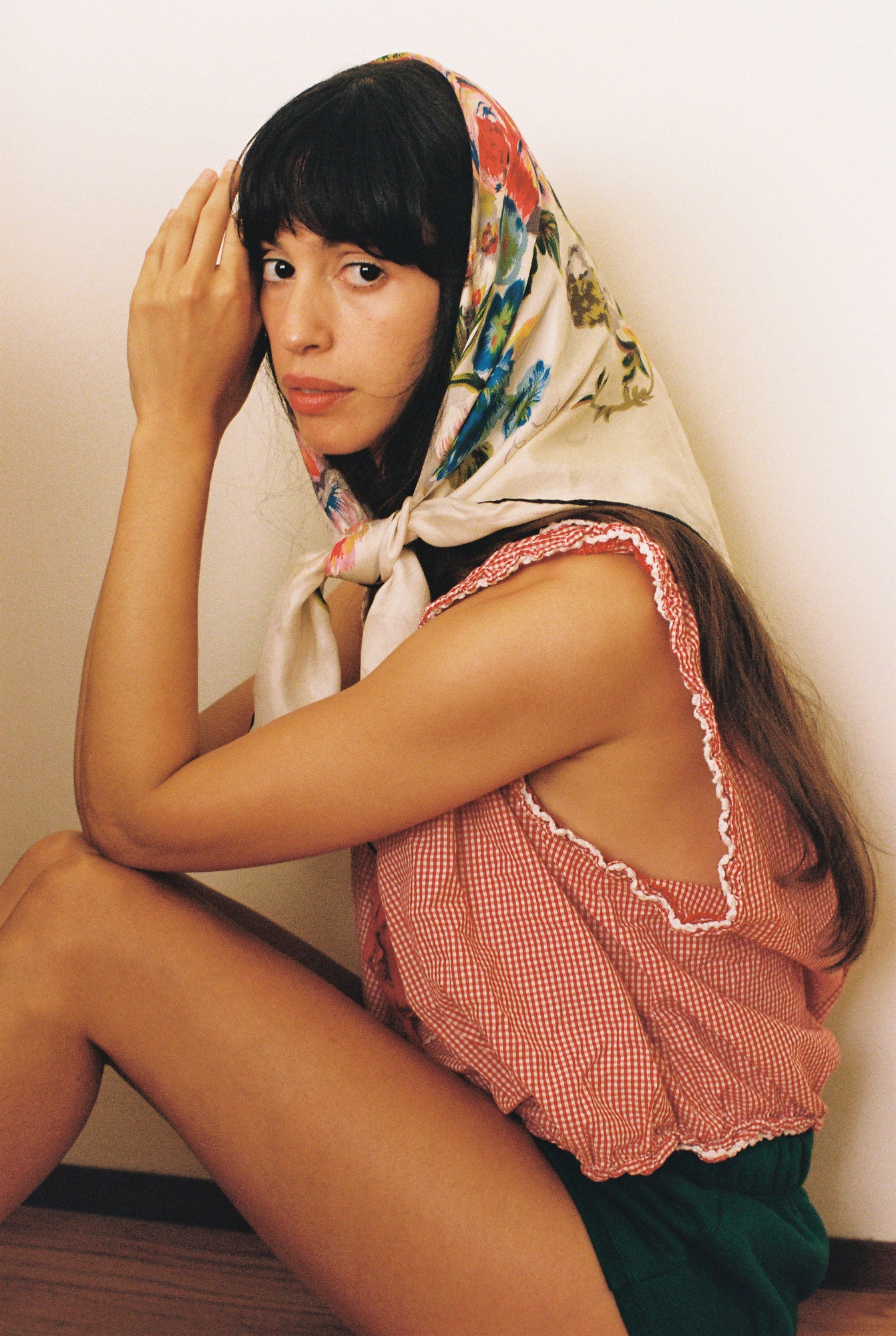 Woman wearing a floral headscarf and pink top sitting against a plain background