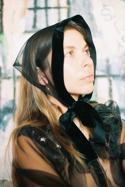 Woman wearing a black sheer bonnet with a large bow in an outdoor setting
