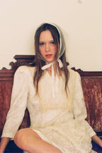 Woman wearing a white lace dress and bonnet sitting on a wooden bench.
