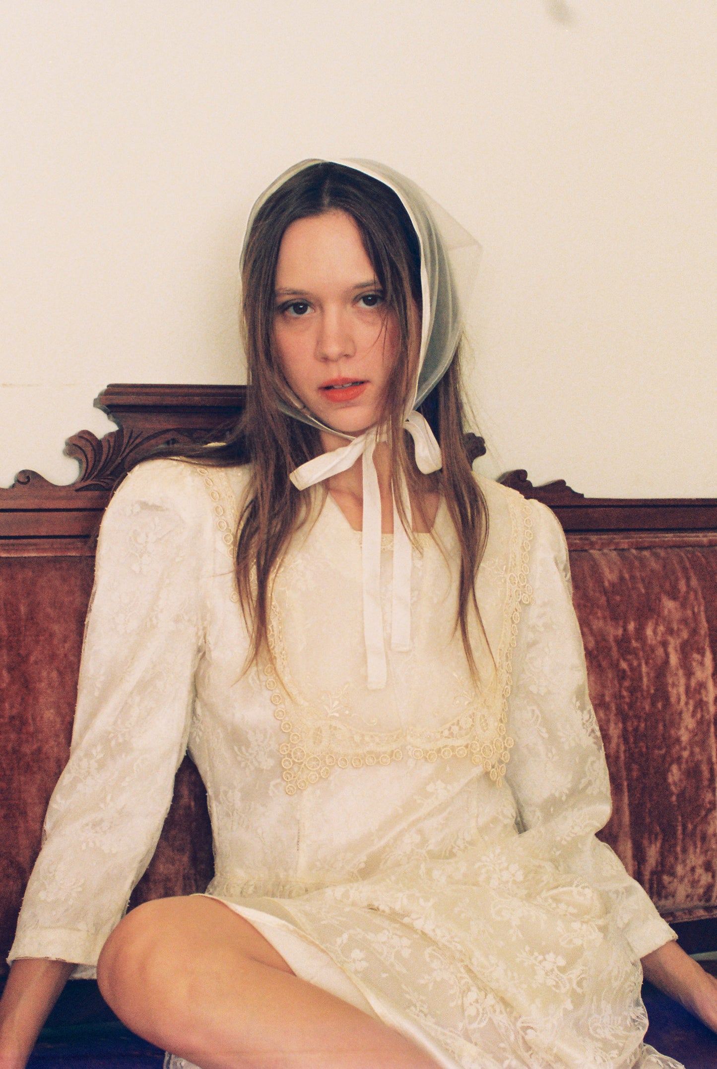 Woman wearing a white lace dress and bonnet sitting on a wooden bench.